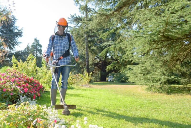 Man in gardening gear and visor performing grounds maintenance with professional lawn mowing tools