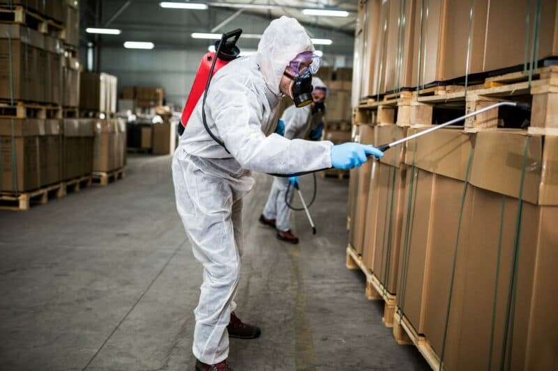 Pest control exterminator in hazmat suit spraying chemicals for pest eradication in commercial warehouse