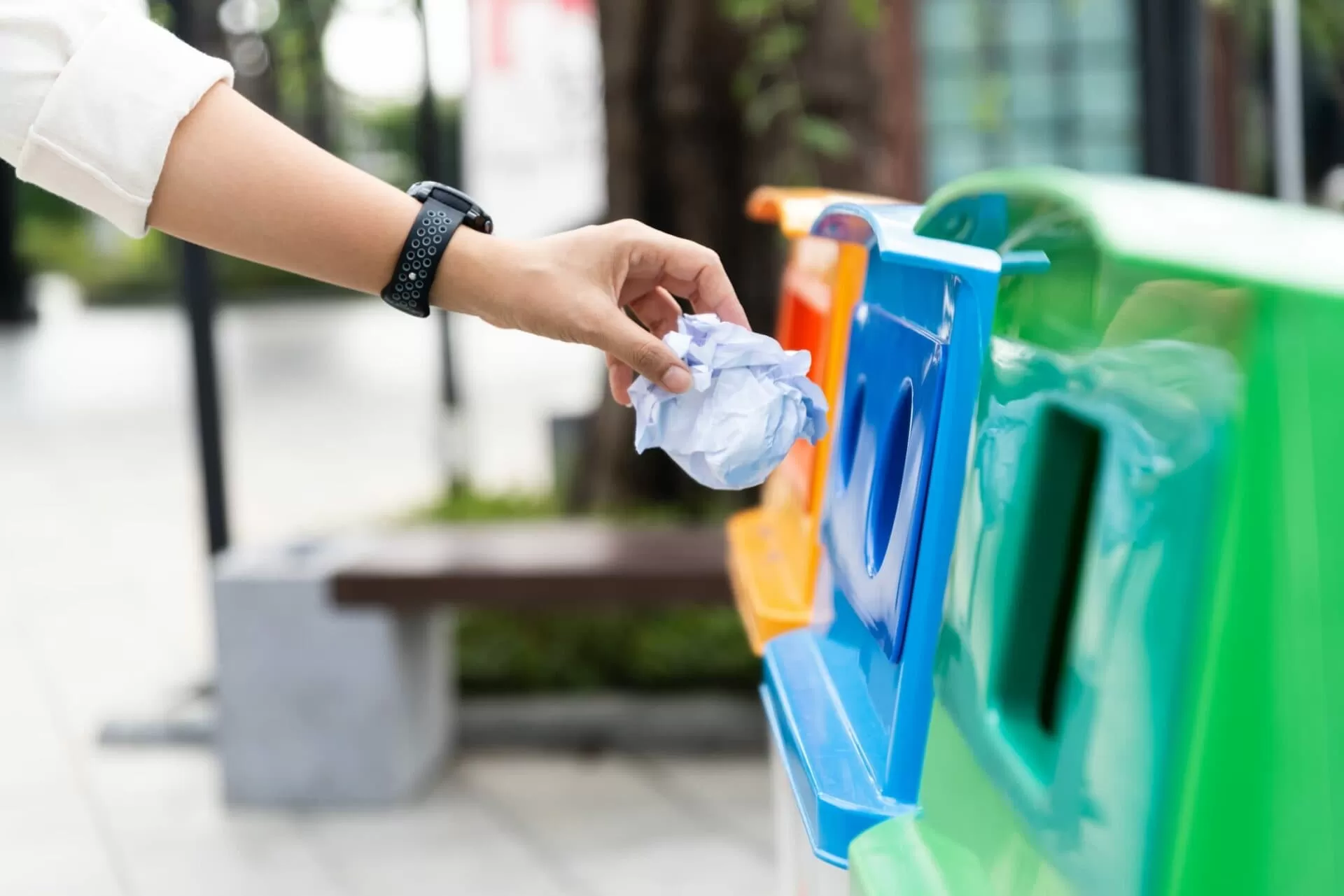 Person using coloured recycling bins to dispose of paper waste