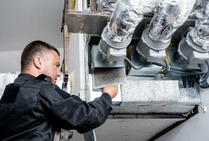 Man cleaning air vents of technical equipment in commercial building