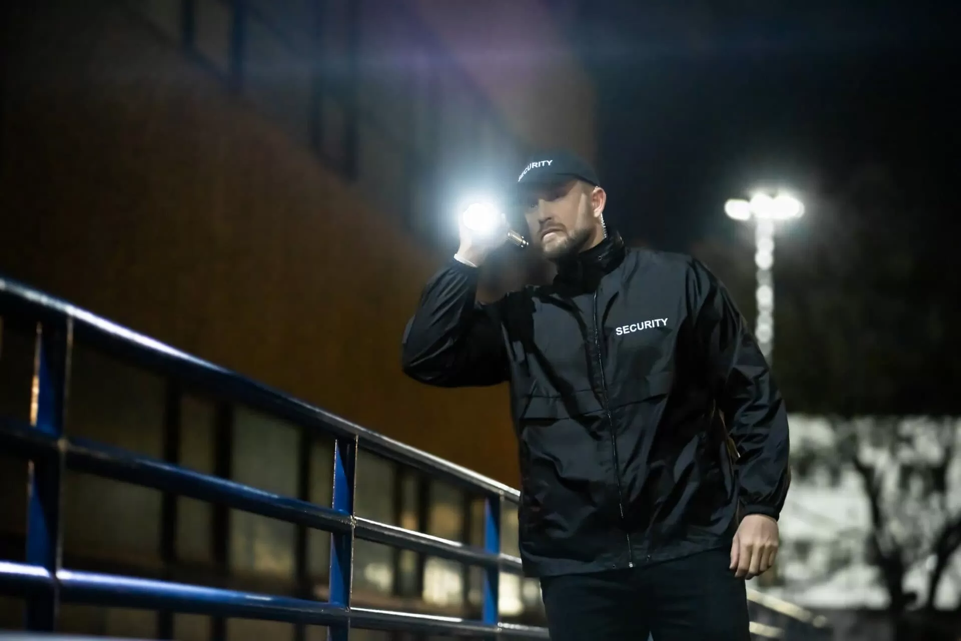 Security guard in all black holding torch while patrolling outdoor commercial space