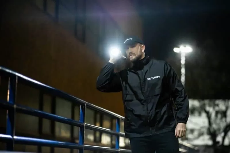 Security guard in all black holding torch while patrolling outdoor commercial space