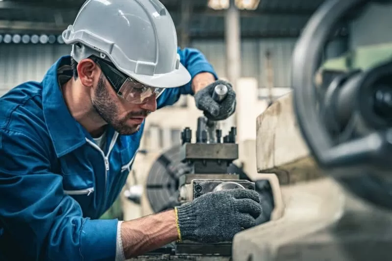 Man in hard hat and protective gear performing maintenance work on tools